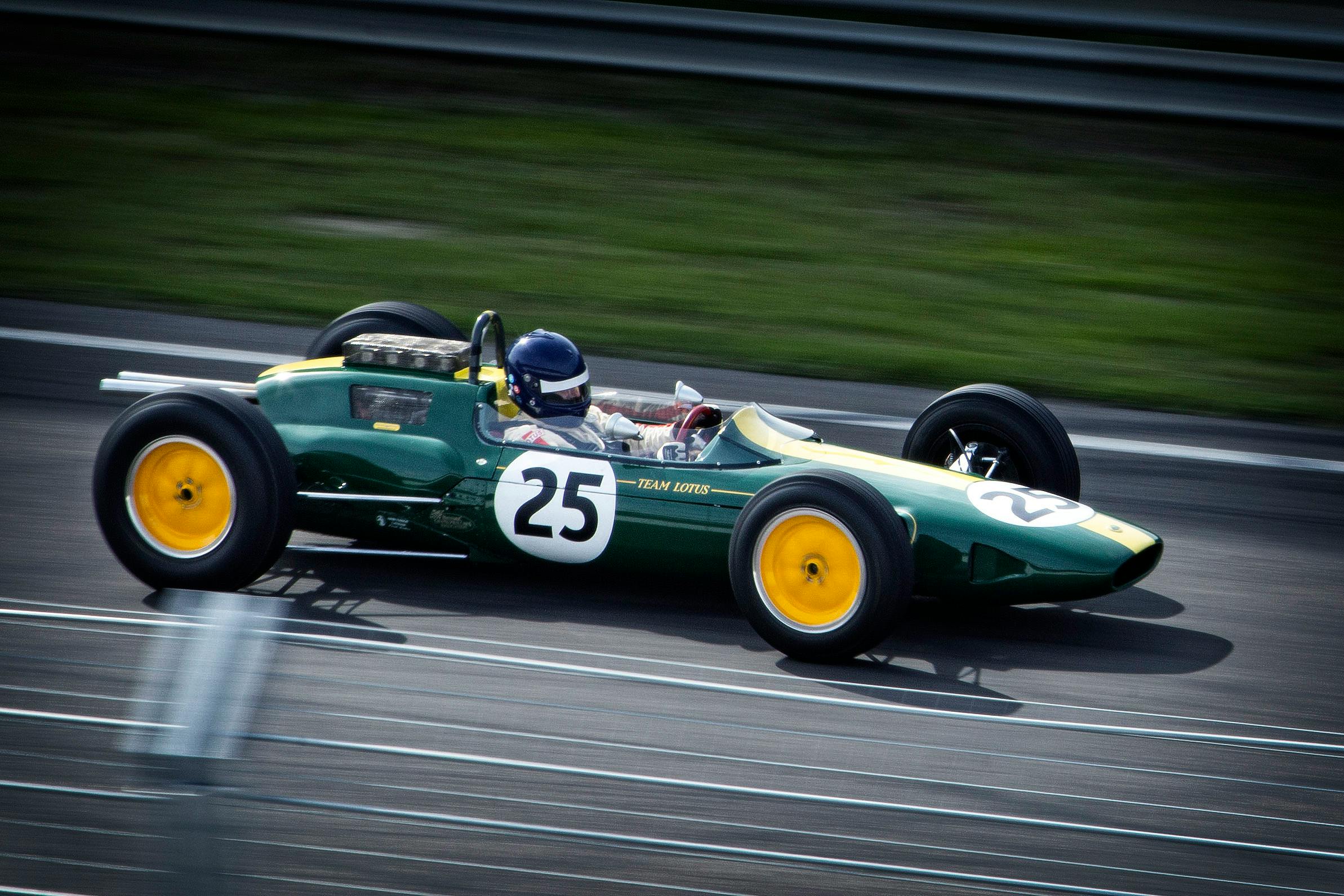 A green vintage Formula 1 car with number 25 speeds around a racetrack, showcasing classic racing heritage.